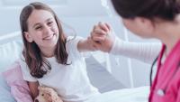 kid holding teddy in hospital bed, high fiving nurse